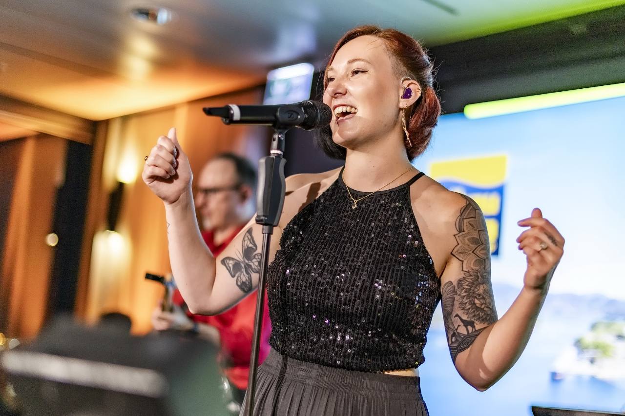 Sängerin der One-Night-Band mit angehobenen Armen und Gitarrist im Hintergrund beim Hamburg-Auftritt